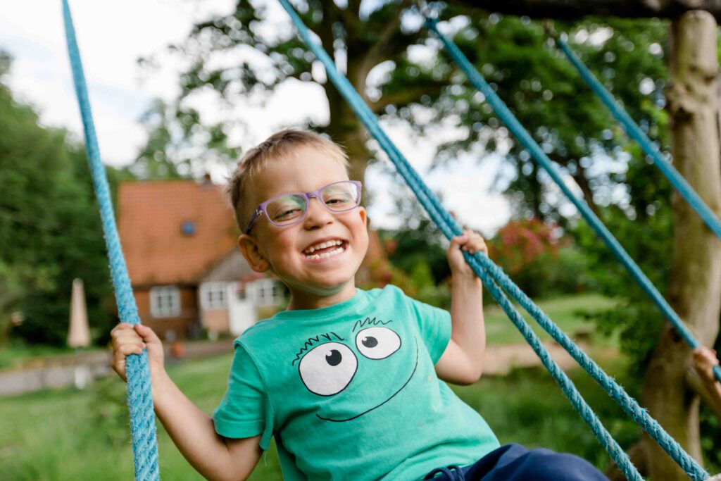 Junge auf Schaukel lächelt in die Kamera - Kindergartenfotografie
