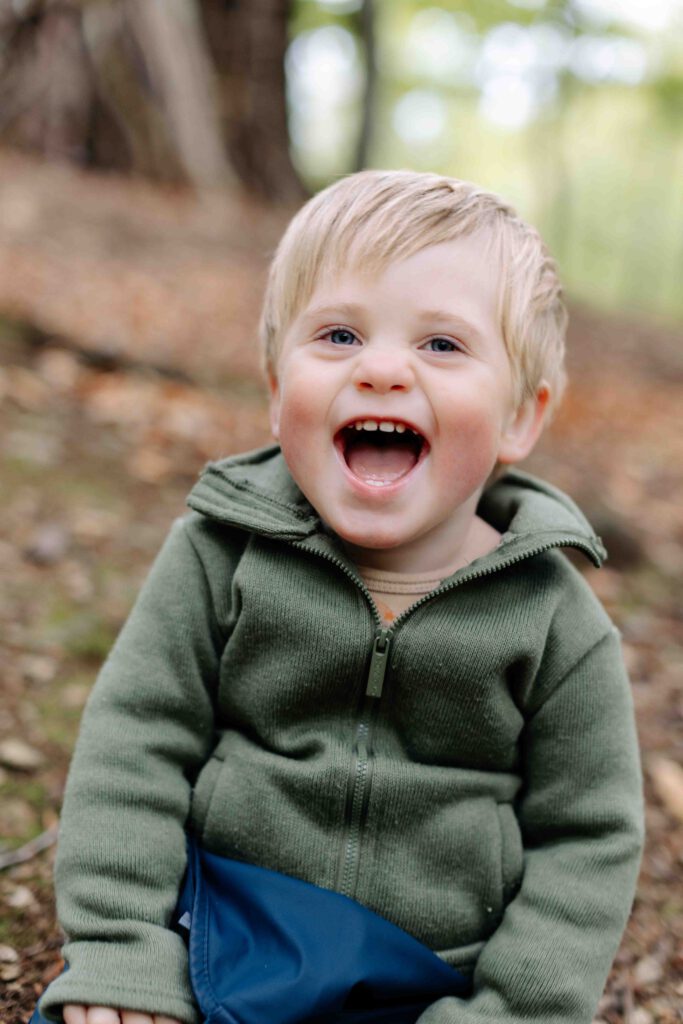 kleiner Junge lächelt herzhaft in die Kamera - Junge im Wald -Kitafotografie
